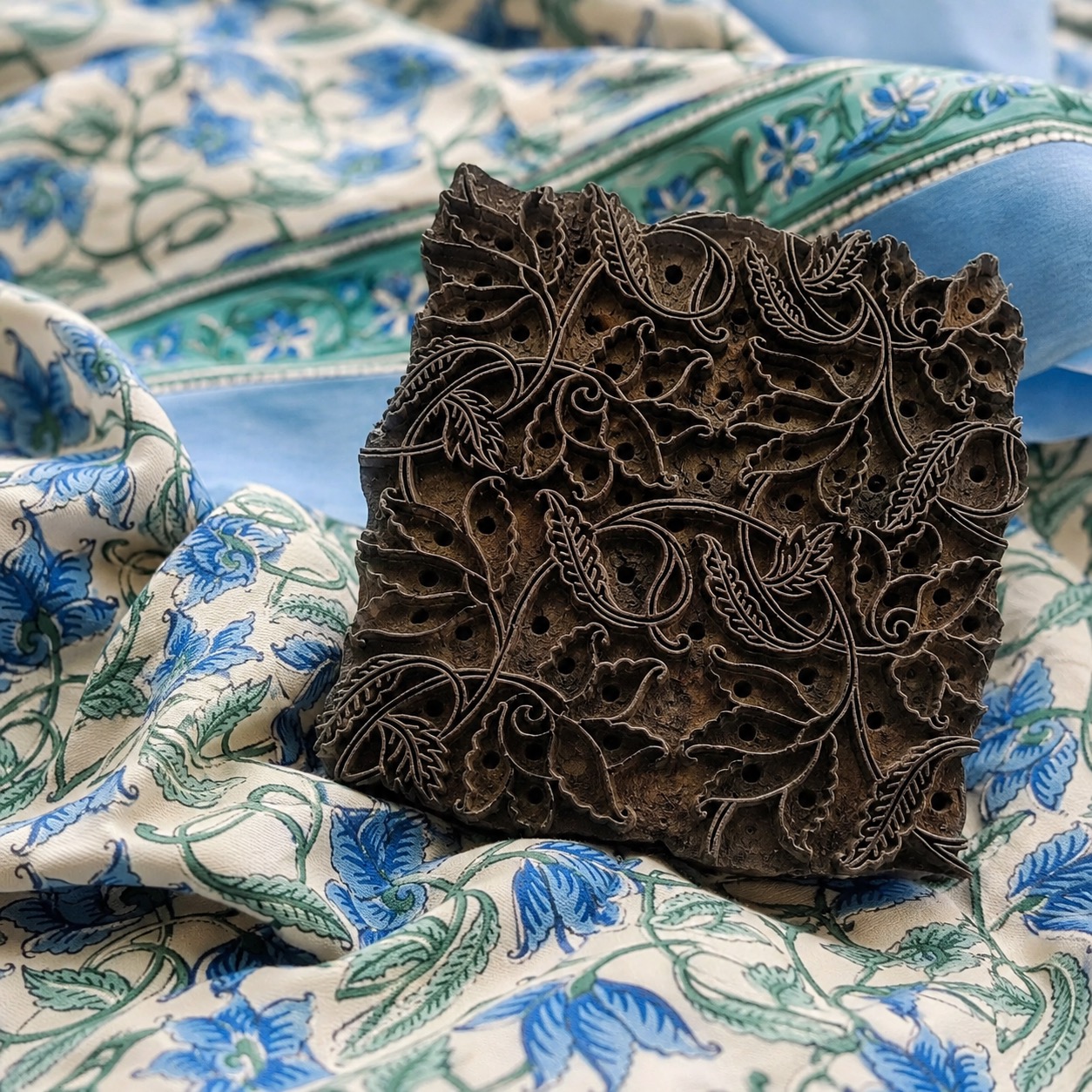 Carved wooden printing block placed on blue floral block printed fabric
