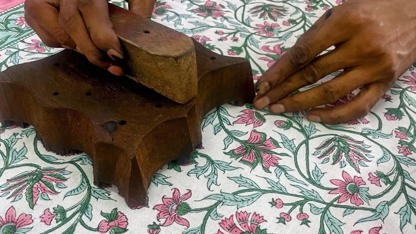 Hands pressing a carved wooden block onto pink-and-green printed cotton